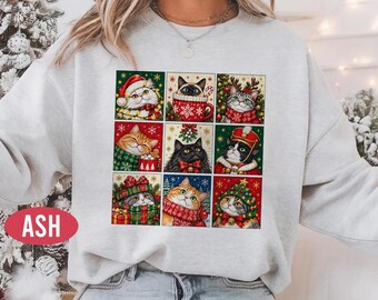 Könnte beinhalten: Ein hellgraues Sweatshirt mit Rundhalsausschnitt und einem Raster aus neun quadratischen Katzenillustrationen in verschiedenen weihnachtlichen Outfits und Umgebungen, darunter Weihnachtsmützen, Schals und Tannenbäume, mit dem Wort ASH in einem roten Oval.