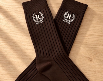 May include: A pair of dark brown ribbed socks featuring a white embroidered emblem with a laurel wreath surrounding the letter R and the name ROBERT printed underneath the letter on the upper portion of each sock.