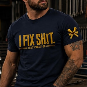 May include: A navy blue short-sleeve t-shirt featuring the yellow text I FIX SHIT. THAT'S WHAT I DO. The sleeve displays a yellow graphic of two crossed wrenches with the name WILLIAM printed across the centre of the tool design.