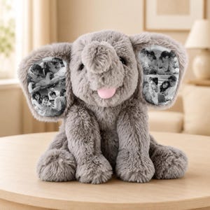 Puede incluir: Un peluche de elefante gris con pelaje suave y una pequeña lengua rosa. El elefante presenta orejas grandes, cada una con un collage de fotografías en blanco y negro que muestran a varias personas en diferentes entornos sociales.