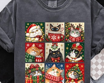May include: A charcoal gray t-shirt featuring a grid of nine festive cat illustrations. The cats are depicted in various holiday scenes, including wearing Santa hats, sitting in mugs, wrapped in scarves, and adorned with Christmas tree decorations.