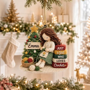 May include: A clear acrylic Christmas ornament featuring a crocheted-style illustration of a person with brown hair crafting next to a decorated tree. The tree has a sign reading Emma. A stack of blocks reads JUST a Girl WHO LOVES Crochets.