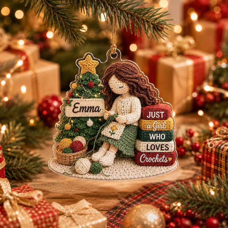 May include: A clear acrylic Christmas ornament featuring a crocheted-style illustration of a person with brown hair crafting next to a decorated tree. The tree has a sign reading Emma, and a stack of books reads JUST a Girl WHO LOVES Crochets.
