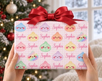 May include: A rectangular gift box wrapped in light pink gingham paper featuring a repeating pattern of colorful, smiling dumpling characters and the name Sophia in cursive script, topped with a large, dark red satin ribbon bow.