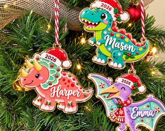 May include: Three flat acrylic Christmas ornaments shaped like dinosaurs, each wearing a Santa hat with the year 2026 printed on it. The green T-Rex is labeled Mason, the pink triceratops is labeled Harper, and the purple pterodactyl is labeled Emma.