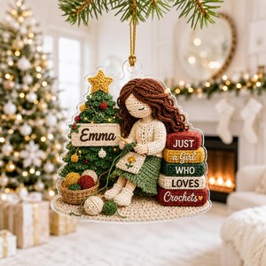 May include: A clear acrylic Christmas ornament featuring a crocheted figure with brown hair sitting next to a green Christmas tree. The tree has a sign reading Emma. A stack of books reads JUST a Girl WHO LOVES Crochets with a small heart.