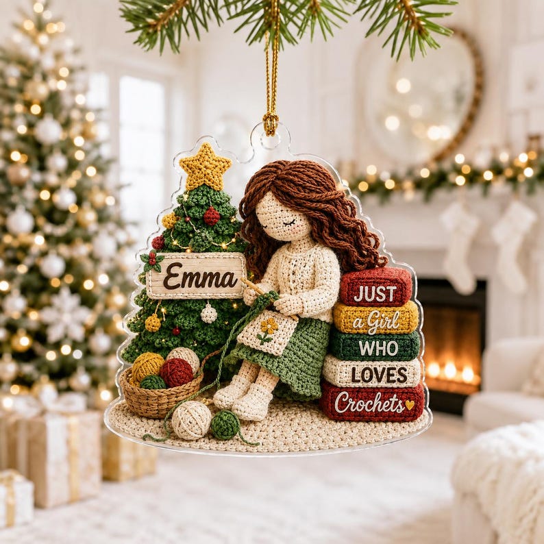 May include: A clear acrylic Christmas ornament featuring a crocheted figure with brown hair sitting next to a green Christmas tree. The tree has a sign reading Emma. A stack of books reads JUST a Girl WHO LOVES Crochets with a small heart.