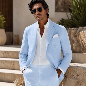 May include: A light blue blazer and matching trousers paired with a crisp white button-down shirt. The blazer features a notched lapel, a single chest pocket with a white pocket square, and dark sunglasses are worn with the ensemble.