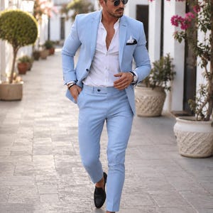 Può includere: Un abito azzurro composto da una giacca monopetto e pantaloni slim fit abbinati, indossato con una camicia bianca con bottoni. La giacca presenta un bavero classico e un fazzoletto da taschino bianco, mentre i pantaloni hanno un taglio dritto.