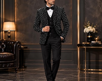 Può includere: Una giacca da smoking nera con un motivo a piccoli pois bianchi, indossata sopra una camicia bianca, un gilet nero e un papillon nero. L'insieme comprende pantaloni neri abbinati e scarpe eleganti nere lucide.