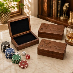 May include: Three rectangular dark wood boxes with black velvet interiors. Two boxes are closed, featuring a laser-engraved deer head, pine trees, and the text Noah Wilson 07.22.2026. One box is open. Poker chips and dice are scattered nearby.