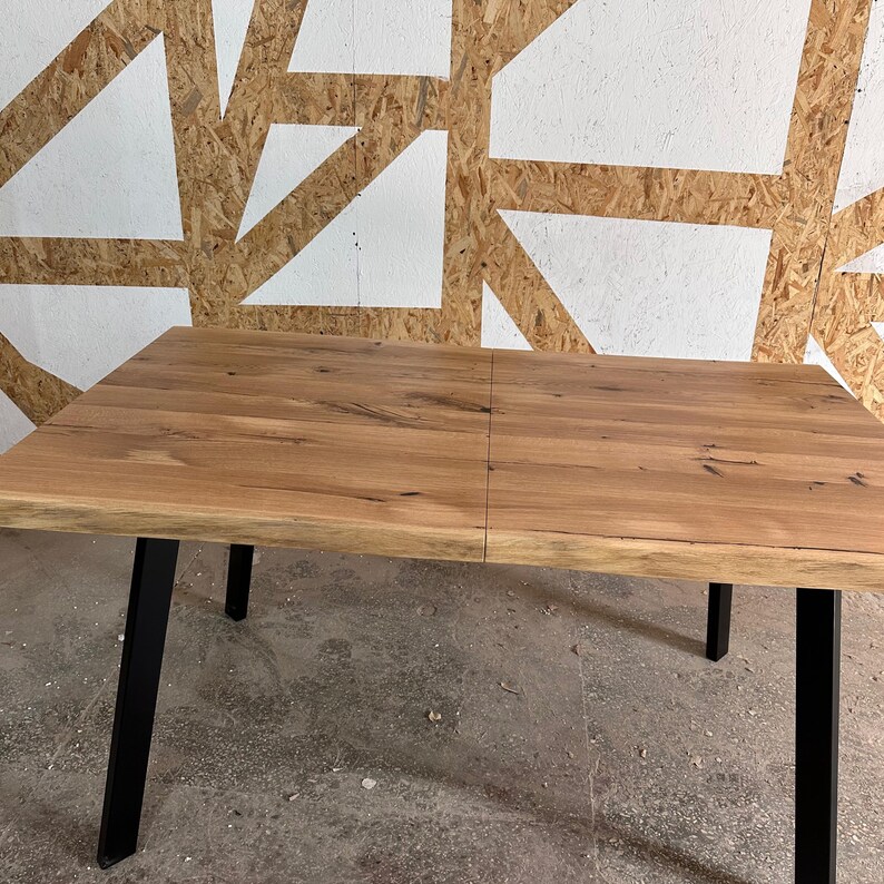 May include: A rectangular dining table featuring a natural light brown wood grain tabletop with a live edge finish. The table is supported by four sturdy, angled black metal legs that provide a stable base for the wooden surface.