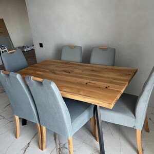 May include: A rectangular dining table with a natural light brown wood grain top and black metal legs, surrounded by six chairs featuring light blue upholstered seats and backrests with light wood accents at the top of each chair back.