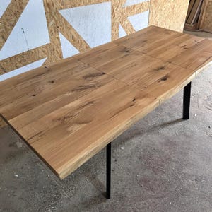 May include: A rectangular dining table featuring a natural light brown wood grain tabletop with visible knots and a smooth finish. The table is supported by four thin, straight black metal legs positioned at each corner of the rectangular frame.