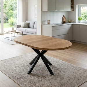 Puede incluir: Una mesa de comedor ovalada con una superficie de madera de color marrón claro con veteado y una base de metal negro con cuatro patas entrecruzadas que forman una X. La superficie de la mesa es lisa y plana, sostenida por una estructura metálica.