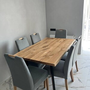 May include: A rectangular dining table with a natural light brown wood grain top and black metal legs, surrounded by six gray upholstered chairs featuring light wood accents on the top of the backrests, arranged in a modern interior space.