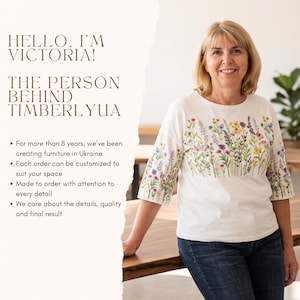 K&ouml;nnte beinhalten: Ein wei&szlig;es T-Shirt mit einem bunten Blumenmuster auf der Brust und den &Auml;rmeln. Das Bild enth&auml;lt den Text: HELLO, I'M VICTORIA! THE PERSON BEHIND TIMBERLYUA. Seit &uuml;ber 8 Jahren fertigen wir M&ouml;bel in der Ukraine. Jede Bestellung ist individuell anpassbar.