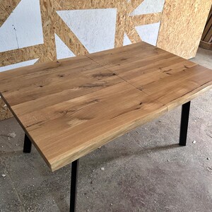 May include: A rectangular dining table featuring a natural light brown wood grain tabletop with visible knots and a live edge. The table is supported by four straight, black metal legs positioned at each corner, providing a stable base for the surface.