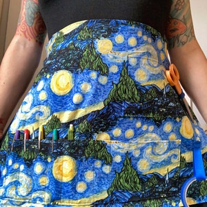 May include: A blue and yellow apron with a print of Van Gogh's Starry Night. The apron has multiple pockets and is perfect for holding art supplies.