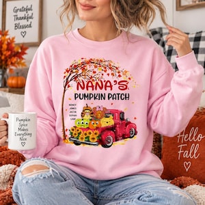 May include: A light pink crewneck sweatshirt featuring a graphic of a red truck carrying pumpkins and sunflowers under a tree. The text reads NANA'S PUMPKIN PATCH with a list of names. A white mug with the text Pumpkin Spice Makes Everything Nice.