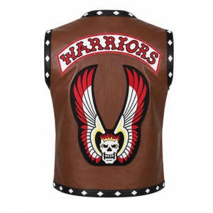May include: A brown leather waistcoat featuring a large embroidered patch on the back with a skull, wings, and the text WARRIORS in red letters. The waistcoat has black trim along the edges decorated with a repeating pattern of small white diamond shapes.