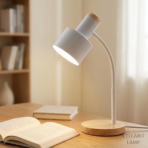 May include: A white desk lamp with a cylindrical head and a light-colored wooden base. The lamp features a flexible white neck and a wooden accent on the top of the lamp head. The text VELLARO LAMP is printed in the bottom right corner of the image.