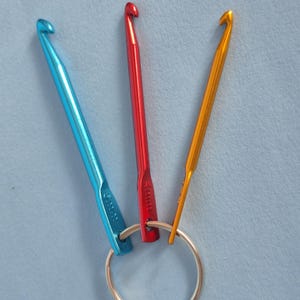 May include: Three metal crochet hooks in blue, red, and gold colors attached to a circular silver metal ring. The blue hook is marked 5.0mm, the red hook is marked 4.0mm, and the gold hook is marked 2.0mm. Each hook features a standard hooked tip.