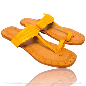 Peut inclure: Une paire de sandales en cuir jaune vif dotées d'une semelle plate, d'une large bride sur le cou-de-pied avec des bords festonnés décoratifs et d'une fine bride verticale reliée à un anneau d'orteil pour maintenir le gros orteil en place.