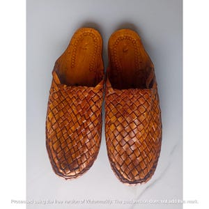May include: A pair of tan leather slip-on shoes featuring a woven upper design. The interior footbed is made of smooth leather with a stamped circular pattern and the number 7 visible near the heel area of each shoe, showcasing a classic construction.