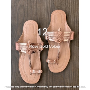 May include: A pair of rose gold sandals featuring a toe post design, a wide metallic strap with intricate embossed detailing, and a flat sole with stitched edges. The text 12 and Rose Gold Colour are visible on the image surface.