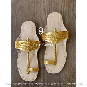 Op de afbeelding: Een paar platte sandalen met een lichtbeige zool en een metallic gouden bovenband met ingewikkelde reli&euml;fpatronen. Het ontwerp bevat een teenring en een brede decoratieve band over de voet. De tekst 9 en Gold Colour zijn zichtbaar.