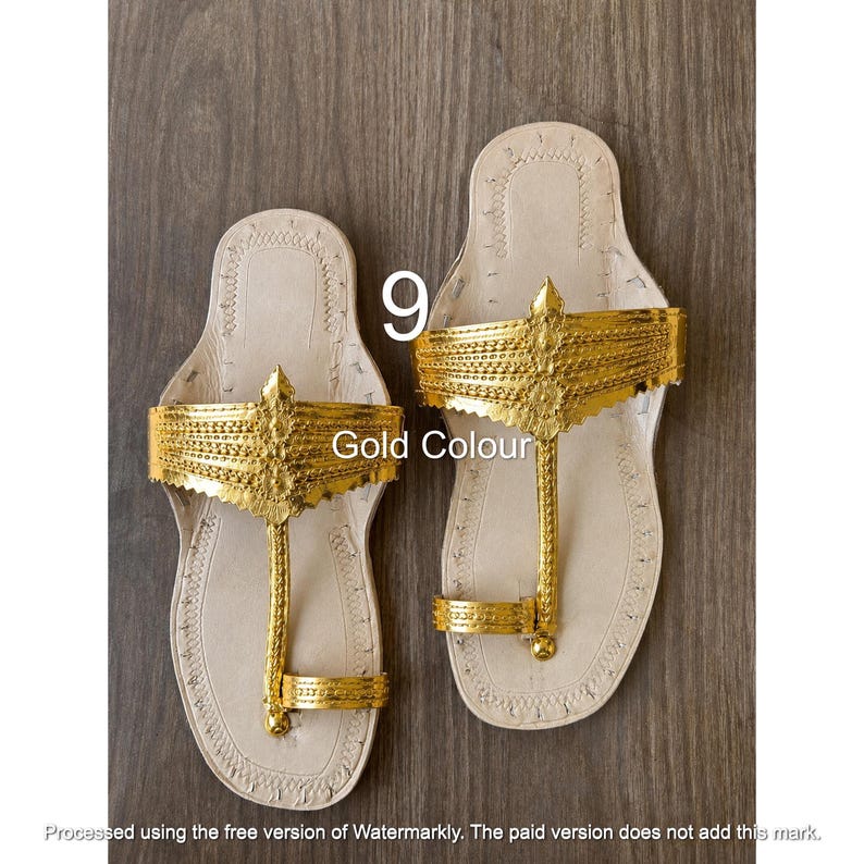 Op de afbeelding: Een paar platte sandalen met een lichtbeige zool en een metallic gouden bovenband met ingewikkelde reli&euml;fpatronen. Het ontwerp bevat een teenring en een brede decoratieve band over de voet. De tekst 9 en Gold Colour zijn zichtbaar.