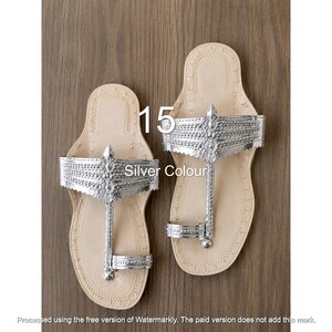 Op de afbeelding: Een paar zilverkleurige sandalen met een teenring en een brede, gestructureerde band over de wreef. Het voetbed is lichtbeige met decoratieve stiksels langs de randen. De tekst 15 en Silver Colour zijn zichtbaar op de afbeelding.