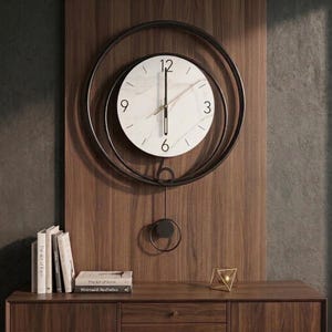 May include: A round wall clock featuring a white marble-patterned face with black numerals at the 12, 3, 6, and 9 positions. The clock is framed by two concentric black metal rings and includes a black pendulum with a circular weight at the bottom.