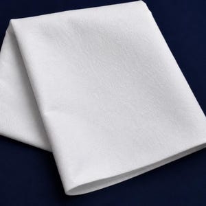 Puede incluir: Una pieza de tela blanca doblada con una textura suave y mate. El material es opaco y limpio, presentando bordes afilados y nítidos donde se pliega sobre sí mismo. La superficie parece uniforme y consistente, sin patrones ni costuras visibles.