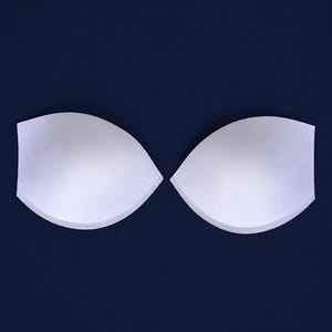 May include: A pair of white, molded foam bra cups with a smooth, rounded shape. These lightweight, contoured inserts are designed for garment construction and provide a structured, supportive form for various types of clothing and apparel.