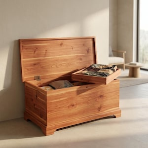 Puede incluir: Un baúl de almacenamiento rectangular de madera con una tapa abatible en posición abierta. El baúl presenta un acabado de veta de madera natural con nudos visibles. Una bandeja de madera extraíble descansa en el borde superior.