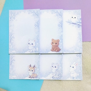 Puede incluir: Juego de seis blocs de notas con temática invernal. Cada bloc de notas presenta una ilustración de un animal diferente: un zorro blanco, un oso pardo, un búho, un ciervo, un leopardo de las nieves y un conejo blanco. Los blocs de notas tienen un borde azul claro y blanco con copos de nieve.