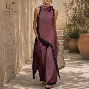 May include: A sleeveless, deep plum-coloured tunic dress featuring a high cowl neckline and a contrasting black trim along the edges. The garment has a long, asymmetrical side panel that drapes down to the hem, creating a layered, flowing silhouette.