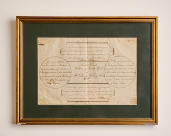 May include: A framed document featuring handwritten cursive text in brown ink on aged, off-white paper. The document is enclosed in a dark green mat and a gold-toned frame. The text is arranged in geometric shapes, including circles and rectangles.