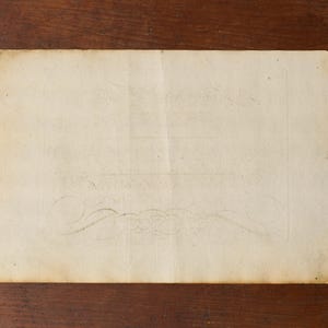May include: A rectangular piece of aged, off-white paper with a weathered texture and uneven edges. The surface displays faint, decorative scrollwork patterns and subtle brown staining, suggesting age and historical use of the material.
