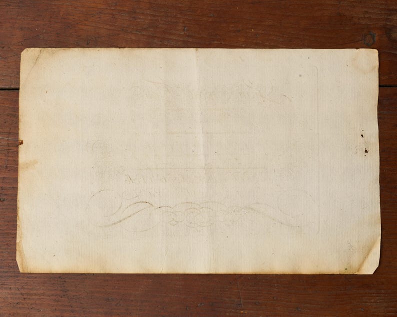 May include: A rectangular piece of aged, off-white paper with a weathered texture and uneven edges. The surface displays faint, decorative scrollwork patterns and subtle brown staining, suggesting age and historical use of the material.