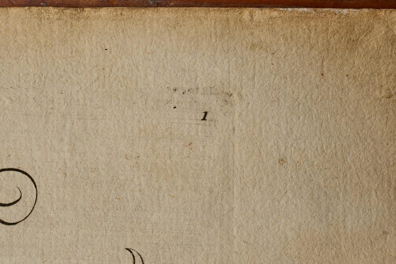 May include: A textured, off-white, aged paper surface featuring a small, black, printed number 1 centered in the upper portion. The paper displays visible fibers, subtle creases, and a dark, weathered edge along the top border of the frame.