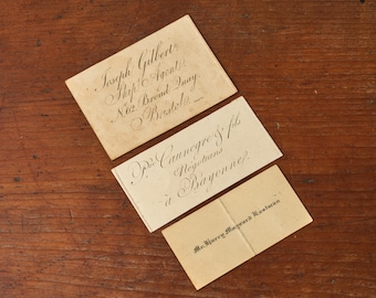 May include: Three rectangular off-white paper cards with black ink calligraphy. The top card reads Joseph Gilbert, Ship Agent, No. 62 Broad Quay, Bristol. The middle card reads Pie Caunegre & fils, Négocians à Bayonne. The bottom card reads Mr. Hjurry Marquard Eusturan.
