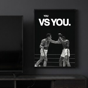 Peut inclure: Une impression d'art murale encadrée en noir et blanc représentant un match de boxe entre deux athlètes sur un ring. Le texte 'YOU VS YOU.' est imprimé en lettres capitales blanches en gras en haut de l'image, au-dessus des deux boxeurs.