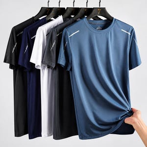 May include: A collection of five short-sleeved athletic t-shirts hanging on black hangers. The shirts are available in black, navy blue, white, dark gray, and blue. Each shirt features a crew neckline and a small reflective silver stripe on the shoulder.