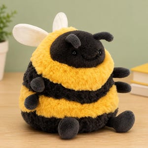 May include: A round, plush bee toy featuring alternating horizontal stripes of fuzzy black and golden yellow fabric. The stuffed animal has two small antennae, two white felt wings on its back, and four small limbs extending from its sides.