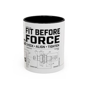 Peut inclure: Un mug en céramique blanche avec un intérieur noir arborant une impression technique noire. Le texte indique FIT BEFORE FORCE, CHECK, ALIGN, TIGHTEN, accompagné de schémas mécaniques, d'étiquettes de mesure et de références d'alignement.