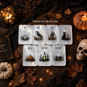 May include: Seven rectangular white tiles featuring illustrations of a ghost, raven, lantern, cat, pumpkin, potion bottle, and cauldron. Each tile displays a letter or word including N, W, E, S, RED, GREEN, and SOAP, arranged in two rows.