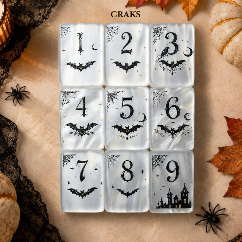 May include: A set of nine rectangular white tiles arranged in a grid, each featuring a black number from one to nine, a bat illustration, and small decorative elements like spiderwebs, stars, and moons. The word CRAKS is printed at the top.